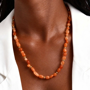 Detail of orange natural stone and gold bead necklace on a model for vacation style