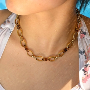 Dettaglio della collana a maglie dorate con perle in resina ambrata sul collo di un modello