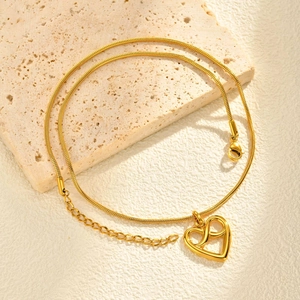 Detail of gold snake chain necklace with hollow heart pendant on natural stone base