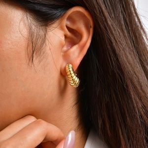 Close-up of golden hollow C-shaped hoop earrings with textured thread design on ear