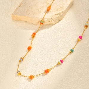 Collier doré en acier inoxydable avec perles colorées sur fond crème texturé