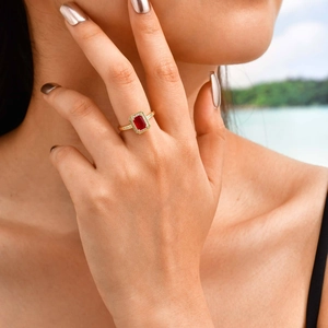 Close-up of a gold ring with rectangular red zircon and halo diamonds on a hand