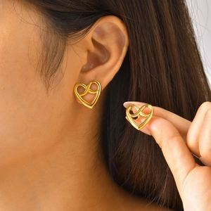 Close-up of a minimalist hollow heart stud earring in a gold finish worn by a model