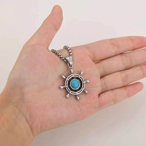 Macro detail of nautical rudder pendant with center turquoise stone on steel chain