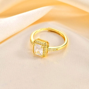 Detail of adjustable gold ring with emerald-cut zirconia and halo setting on satin background