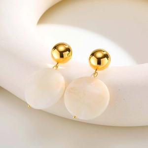 Détail des boucles d'oreilles boules dorées avec disques en résine crème sur un support