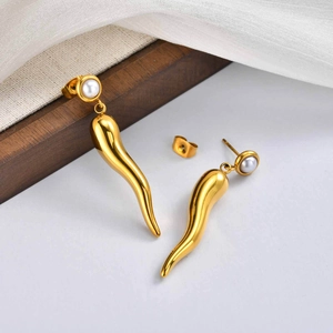 Detail of gold horn drop earrings with pearl stud on soft white fabric background
