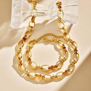 Set minimalista di collana e bracciale dorati con maglie in resina marrone su beige