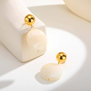 Boucles d'oreilles boules dorées et résine crème marbrée sur un support blanc géométrique