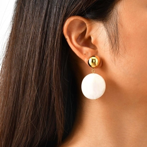 Détail de boucles d'oreilles rondes en résine blanche et bille dorée polie