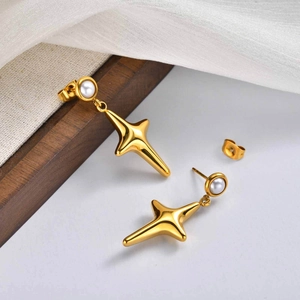 Detailed close-up of golden four-pointed star earrings with white pearls on linen background