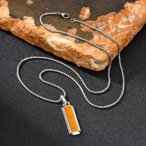 Detailaufnahme des Tigerauge-Anhängers an Edelstahlkette auf rustikalem Felsen