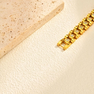 Detailed shot of golden watch-band style bracelet with inlaid zircons on travertine stone