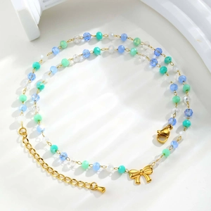 Détail du collier de perles dégradées bleues avec breloque nœud doré sur fond blanc