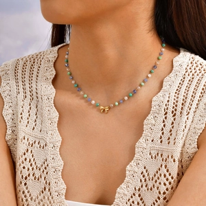 Collier de perles colorées pour femme avec pendentif nœud doré porté par un mannequin