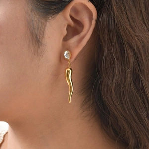 Detail of gold teardrop zircon horn earrings showing a polished drop pendant on model
