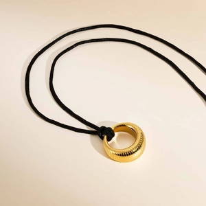 Gros plan du pendentif cercle doré avec texture rayée et cordon en cire noire tressée