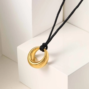 Détail du pendentif doré à texture nervurée sur un collier en cordon noir ajustable