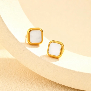 Macro detail of square gold-plated earrings with white mother-of-pearl inlay on stone texture