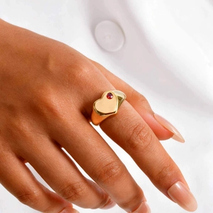 Gros plan d'une bague coeur dorée avec pierre de naissance rouge sur anneau large