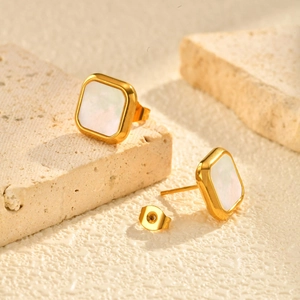 Close-up of golden square stud earrings with white mother-of-pearl inlay on stone