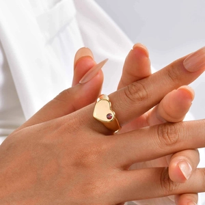 Vue macro d'une bague coeur en or avec pierre de naissance rouge portée par un mannequin
