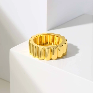 Vue détaillée d'une bague large dorée avec bords festonnés et rainures verticales