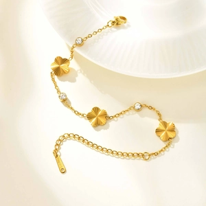 Detail of gold stainless steel bracelet with floral charms and zircon stones on white tray