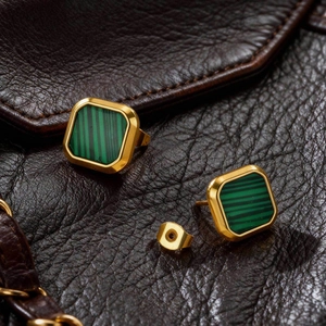 Macro view of square gold earrings with green malachite texture on leather background