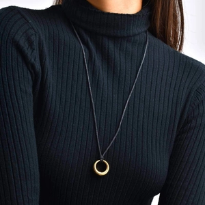 Détail du pendentif anneau doré avec texture radiale sur un pull noir à col montant