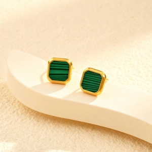 Detailed view of square gold earrings with green malachite stone inlay on a white stand