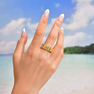 Vue détaillée d'une bague large dorée avec texture rainurée verticale portée par un mannequin