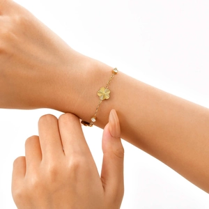 Detail of a gold stainless steel five-leaf flower bracelet with zircons on a woman's wrist