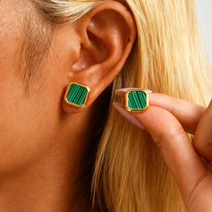 Close-up of golden square stud earrings with green malachite inlay worn by a model