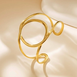 Close-up of golden minimalist double-layer irregular curved open bangle on beige fabric