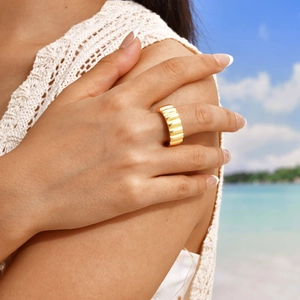 Bague large dorée à texture ondulée au design minimaliste portée sur une plage