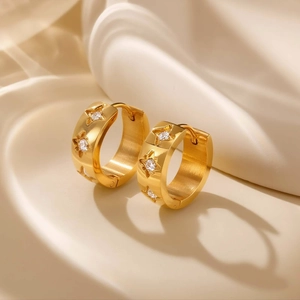Goldene Edelstahl-Ohrringe mit gravierten Sternen und Zirkonia auf Seidenhintergrund