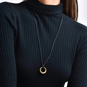 Collier minimaliste avec pendentif circulaire doré et cordon noir porté sur un modèle