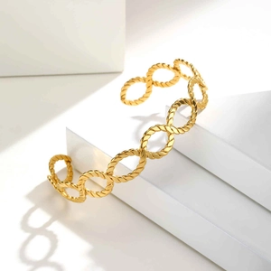 Polished 18K gold-plated twisted cable cuff bangle on white geometric pedestal