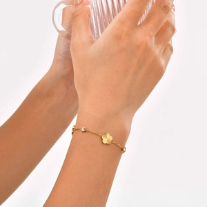 Gold stainless steel flower bracelet with zircon stones worn on a wrist holding a glass