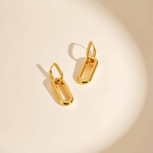 Polished gold geometric oval hoop earrings with interlocking U-shaped links on beige background