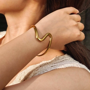 Close-up of a wavy gold stainless steel bangle bracelet on model wearing beige knitwear