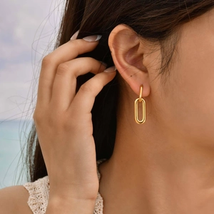 Close-up of elegant gold oval double-loop earrings worn by a model on a sunny beach