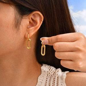 Detail of golden double-loop geometric earrings on model with polished metal finish