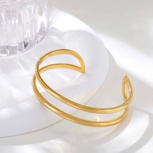 Polished gold double-layer geometric open bracelet on a minimalist white display tray