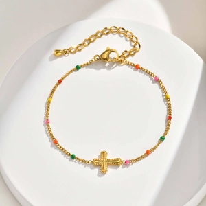 Close-up of gold chain bracelet with colorful beads and cross pendant on white plate