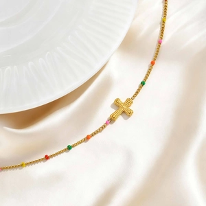 Detail of gold cross pendant necklace with colorful beads on white silk background