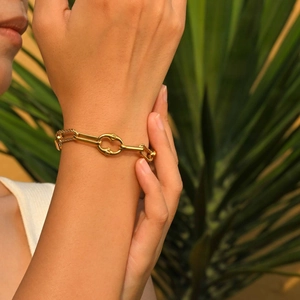 Bracciale a catena dorata al polso su uno sfondo elegante di foglie di palma tropicale