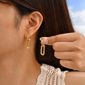 Minimalist gold geometric oval drop earrings worn outdoors against a blue sky