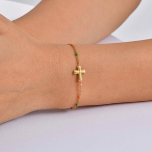 Detailed macro view of a gold cross bracelet with vibrant colorful enamel beads on skin